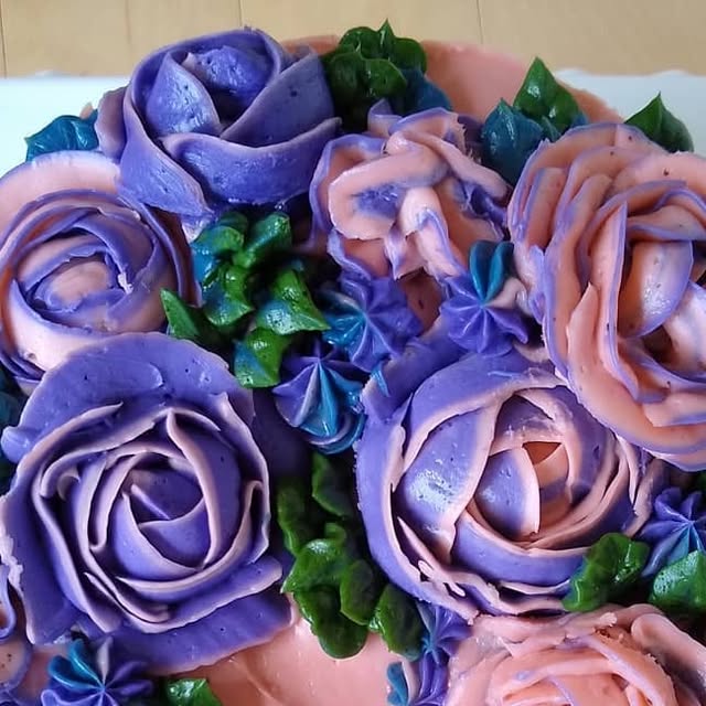 Top view of a cake covered in piped buttercream roses in violet and pink with green leaves